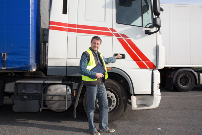 smiling driver with tablet computer, in front of trucks